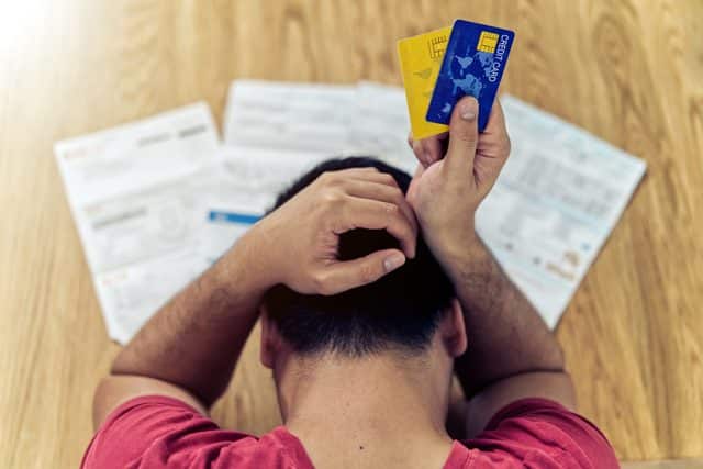 Man holding credit cards sitting at a table stressed about his debts